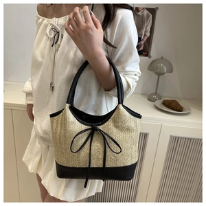 Detail of handwoven straw tote with black leather trim and bow on a white top