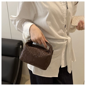 Detail of dark brown snake pattern embossed pillow bag held by model in casual outfit