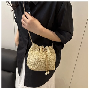 Detail of straw woven bucket bag featuring pearl drawstring and gold chain strap