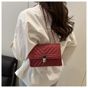Detailed view of deep red quilted cross-body bag with silver metal lock and chain strap