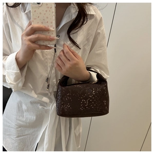 Detail of dark brown mini snake pattern embossed handbag held against a white shirt