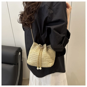 Detail of woven straw bucket bag with gold chain strap and elegant pearl drawstring