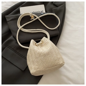 Nahaufnahme der Fischgräten-Struktur einer weißen Strohtasche mit goldener Perle am Seil