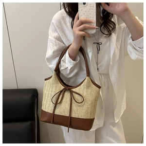Detail of woven straw tote bag with brown leather base and bow decoration