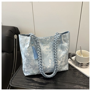Macro detail of light blue tote bag with floral jacquard, braided handle, and tassel charm