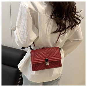 Detail of red quilted crossbody bag with V-shaped stitching and chain strap on model