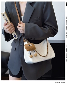 Detail of white soft faux leather shoulder bag with gold chain and plush charm on model