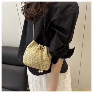 Detail view of woven straw bucket bag with gold chain strap and pearl drawstring tassels
