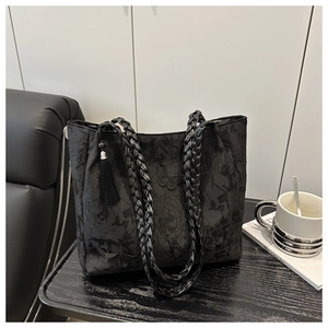 Close-up of black lace tote bag with jacquard fabric, woven handles and tassel detail