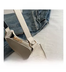Detail view of white lychee leather texture and golden metal hardware on a baguette bag