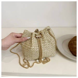 Close-up of beige woven bucket bag with gold chain and decorative pearl drawstring