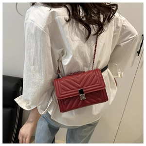 Detailed view of burgundy quilted leather crossbody bag with silver chain strap worn on person