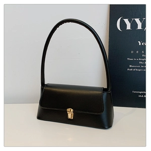 Détail du sac sous l'aisselle en cuir mat noir avec fermoir doré sur fond blanc