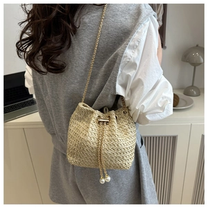 Model wearing a woven bucket bag with gold chain strap and pearl drawstring detail