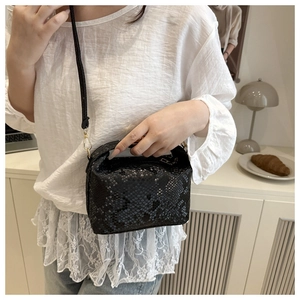 Detail shot of black snakeskin texture shoulder bag on a model in elegant home setting