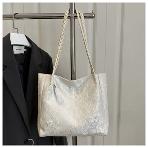 Detail of white lace tote bag featuring 3D butterfly embroidery and a fringe charm