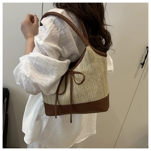 Detail of woven straw tote bag with brown leather trim and bow on a female model