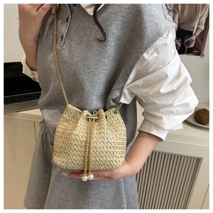 Close-up of woven straw bucket bag with gold chain strap and pearl drawstring detail