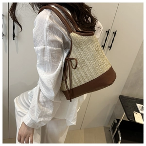 Detail of woven straw tote bag with brown PU leather trim and side bow on model