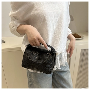 Detail of black snakeskin patterned handbag featuring top handle and metal ring hardware