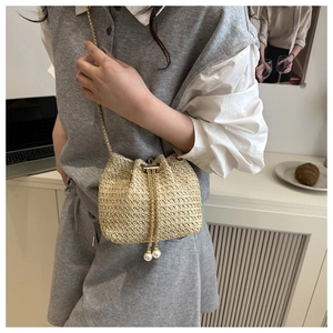 Detail view of beige straw bucket bag with gold chain strap and pearl drawstring closure