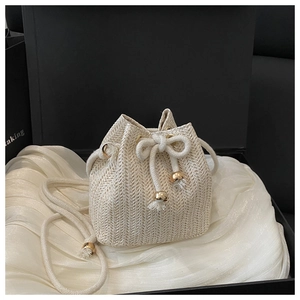 Detail der beigen Stroh-Beuteltasche mit goldenem Kordelzug auf weißem Satin