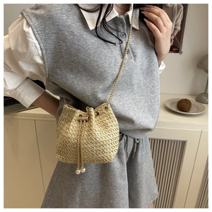 Detailed view of straw bucket bag with gold chain strap and pearl drawstring tassels