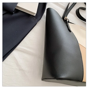 Detail of a tri-color leather tote bag featuring black, cream, and camel panels with slim straps