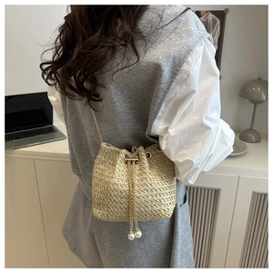 Detail of beige straw bucket bag with gold chain and pearl drawstring on model