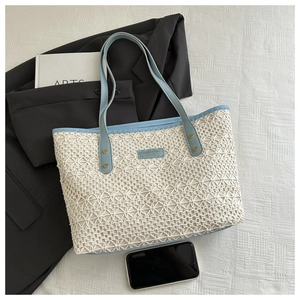 Detail of cream woven tote with blue lace texture, leather logo, and gold rivets