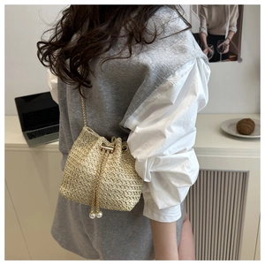 Detail of woven bucket bag featuring drawstring pearls and a gold chain strap
