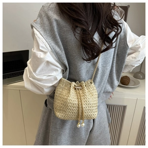 Detail of woven straw bucket bag with gold chain drawstring and pearl charm accents