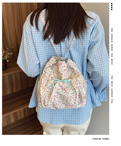 Detail of floral drawstring backpack with plaid bow and pink snap button on canvas fabric