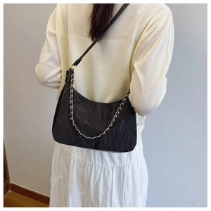 Chic black pleated tote bag with gold chain strap shown on model in a modern style