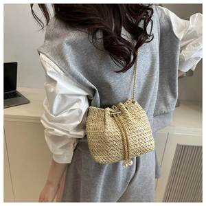 Detail of woven straw bucket bag with gold chain strap and pearl drawstring closure