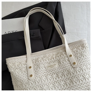 Detail of off-white woven tote bag featuring leather handles and gold rivet accents