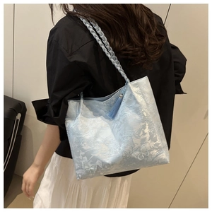 Detail of light blue embossed tote bag with braided handles and decorative tassels on model