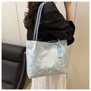 Close-up of light blue tote bag featuring butterfly embroidery and woven shoulder strap