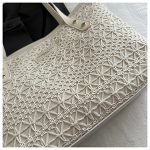 Close-up of white woven tote bag with hollow geometric floral patterns and gold metal studs