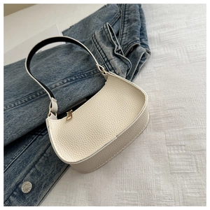Detail der weißen Leder-Struktur auf der Halbmond-Tasche vor einer blauen Jeansjacke