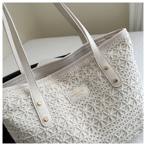 Detail of white woven tote bag featuring reinforced leather handles and a brand tag