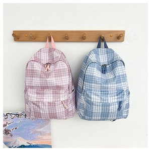 Detailed view of pink and blue checkered backpacks with woven zip pulls hanging on a wall