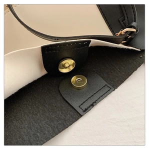 Detail of golden magnetic snap closure and black leather strap on contrast tote bag