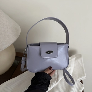 Lavender patent leather shoulder bag with metallic logo on textured white fabric