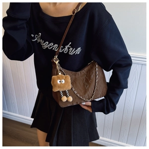 Detail view of brown pleated crescent shoulder bag with metallic chain and plush pendant