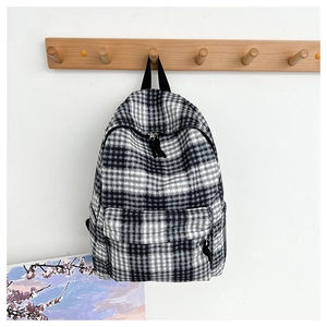 Vertical view of a black and white checkered backpack hanging on a minimalist wood hook
