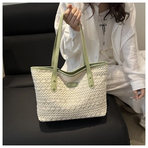 Detail of woven cream tote bag with green handles and branding metal plaque