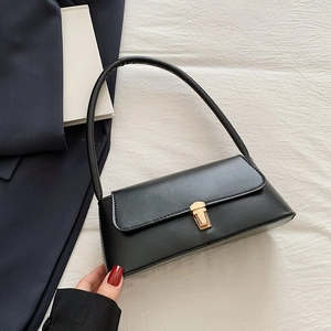 Sac baguette noir minimaliste avec fermoir bouclier doré sur tissu blanc