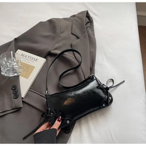 Detail der schwarzen Lackleder-Schultertasche mit silbernen Nieten und seitlichen Schleifen
