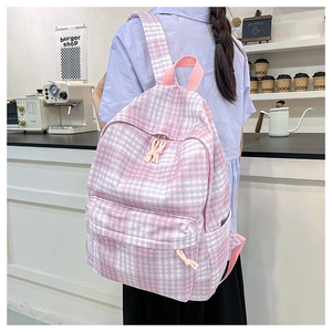 Close-up of pink and white checkered canvas backpack worn by model in a cafe setting